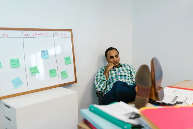 Man in casual attire relaxing at his office desk, contemplating work on a kanban board. Planning marketing automation skills by task
