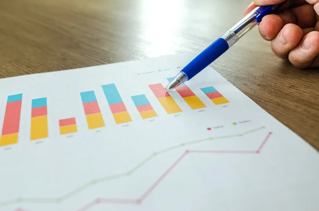 Detailed close-up of a hand pointing at colorful charts with a blue pen on wooden surface. Marketing automation strategy: platform control tests to run