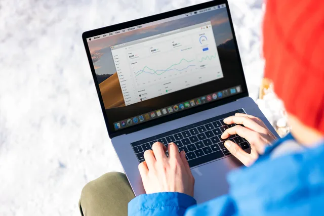 A person in a blue jacket analyzing business analytics on a laptop outdoors during winter. Programmatic advertising surveys: separate Brand Lift from Qualtrics Workflows